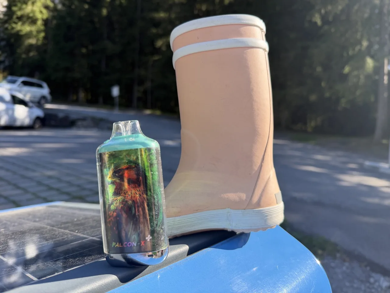 Ein einzelner rosa Kinder-Gummistiefel und eine bunte Einweg-E-Zigarette auf einem Abfalleimer am Parkplatz