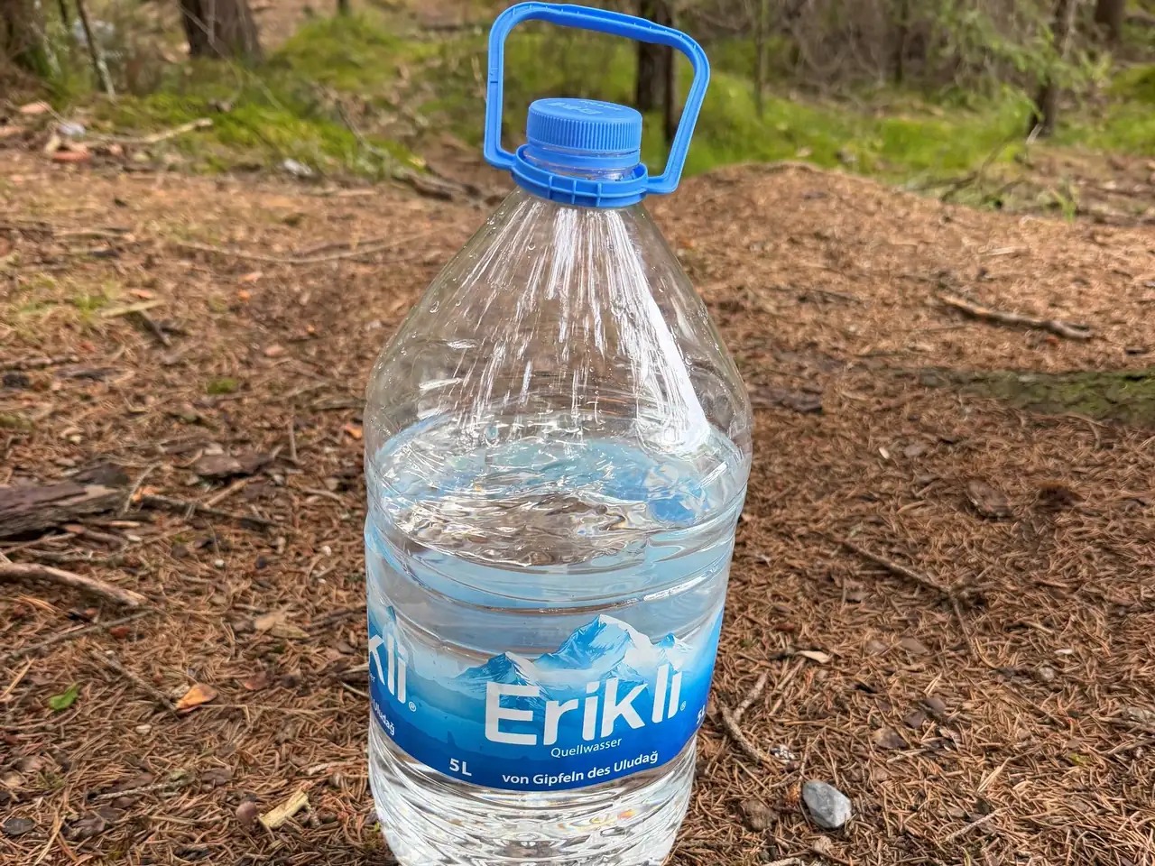 Ein 5-Liter-Wasserkanister, noch zu zwei Dritteln gefüllt, auf dem Waldboden