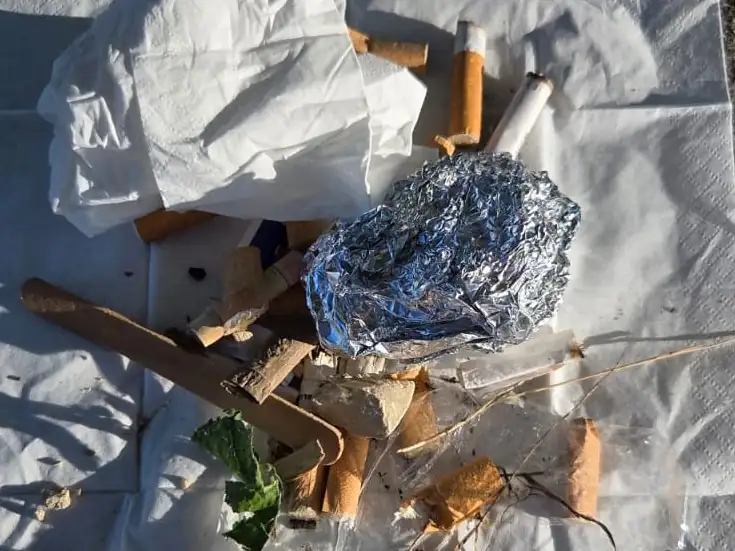 Eingesammelter Abfall auf einer Serviette ausgebreitet: viele Zigarettenstummel, ein Knäuel Alufolie, Papiertaschentücher und ein Holzstiel