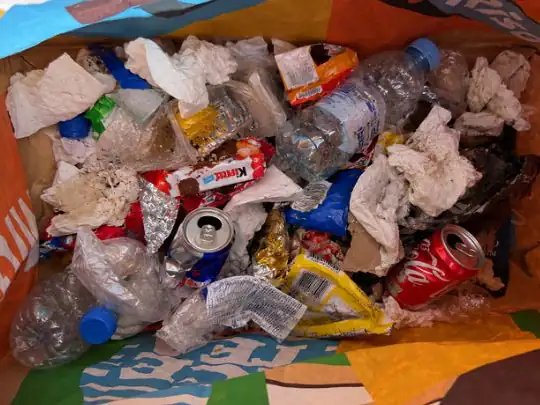 Tragtasche voll eingesammeltem Abfall: PET-Flaschen, Getränkedosen, Schokoladen- und Snackverpackungen, Alufolie und Papiertaschentücher