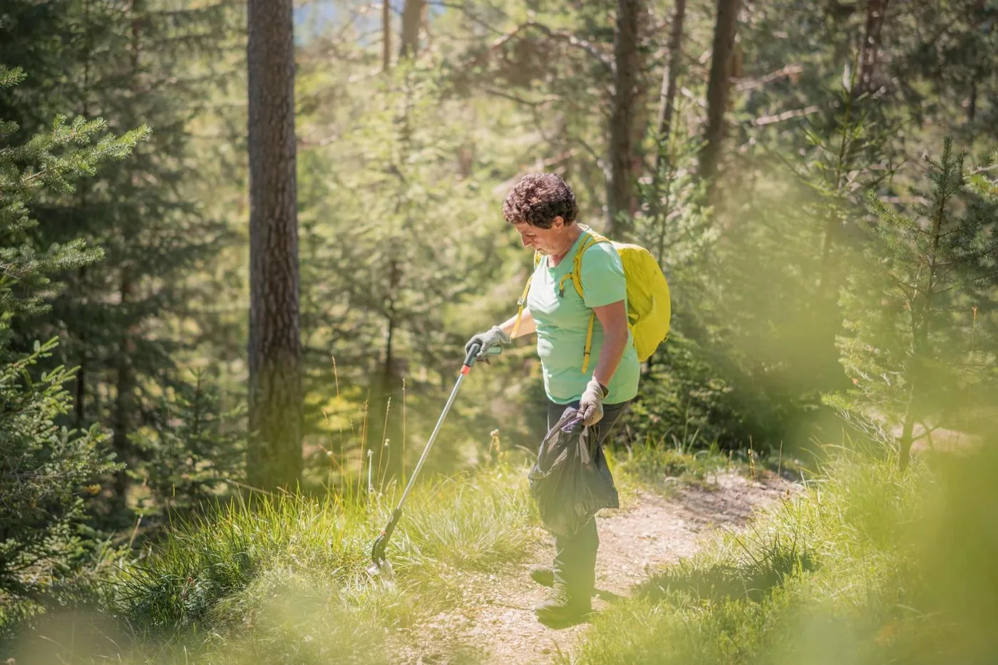 Wanderin sammelt mit einer Greifzange Abfall am Waldweg auf